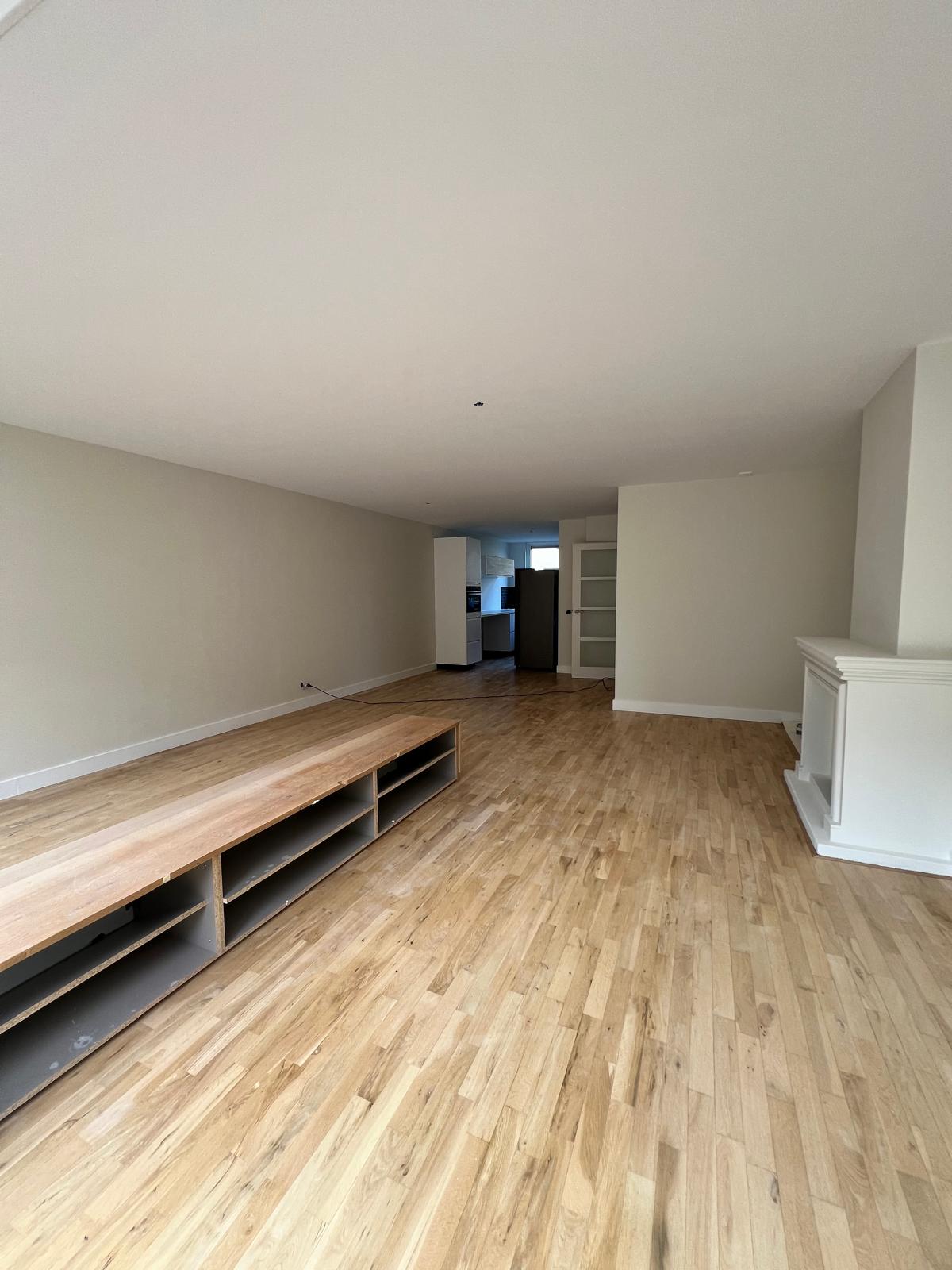 Woonkamer met houten vloer, tv meubel en lichte wanden