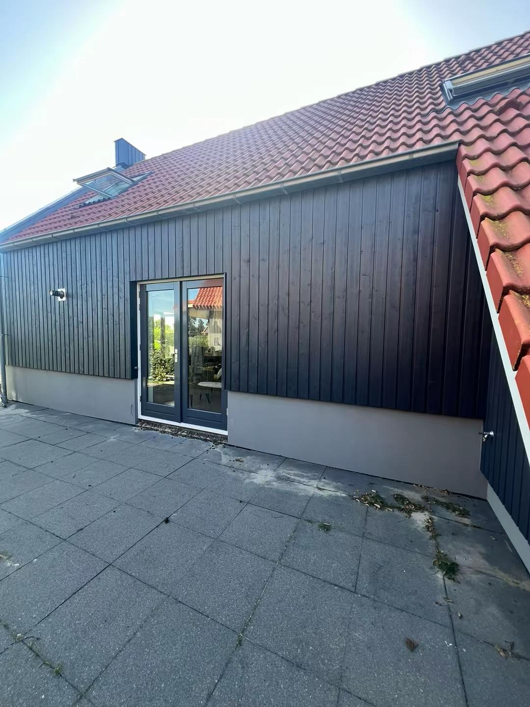 Zijaanzicht van villa met strak afgelakt houtwerk en rode dakpannen